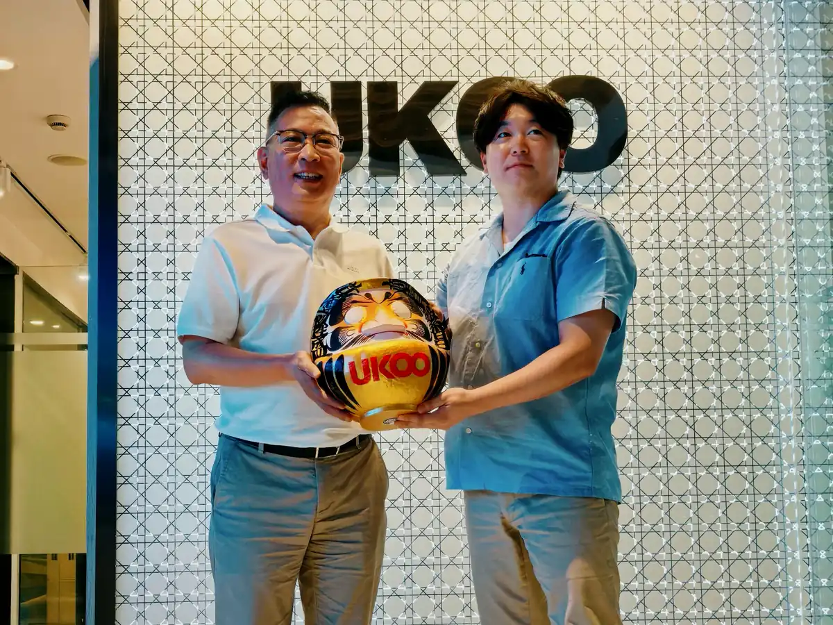 UKOO 本社で、UKOO のロゴを入れた高崎だるまを一緒に持つ両社の代表